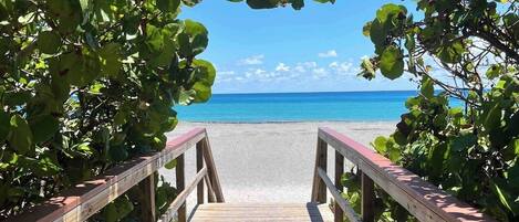 A wooden boardwalk leading to a beach with clear blue water and a sandy shore.