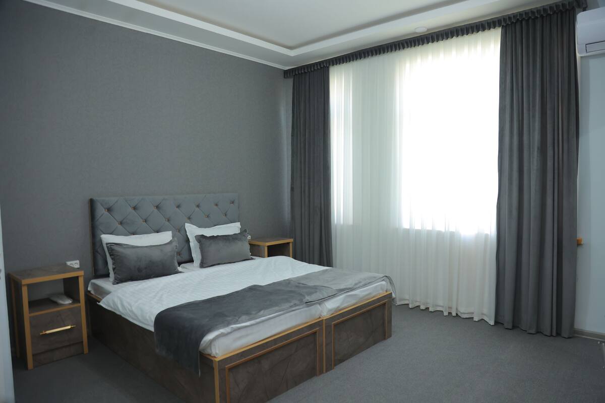 Ein modernes Schlafzimmer mit einem großen Bett, zwei Nachttischen und einem Fenster mit Vorhängen.