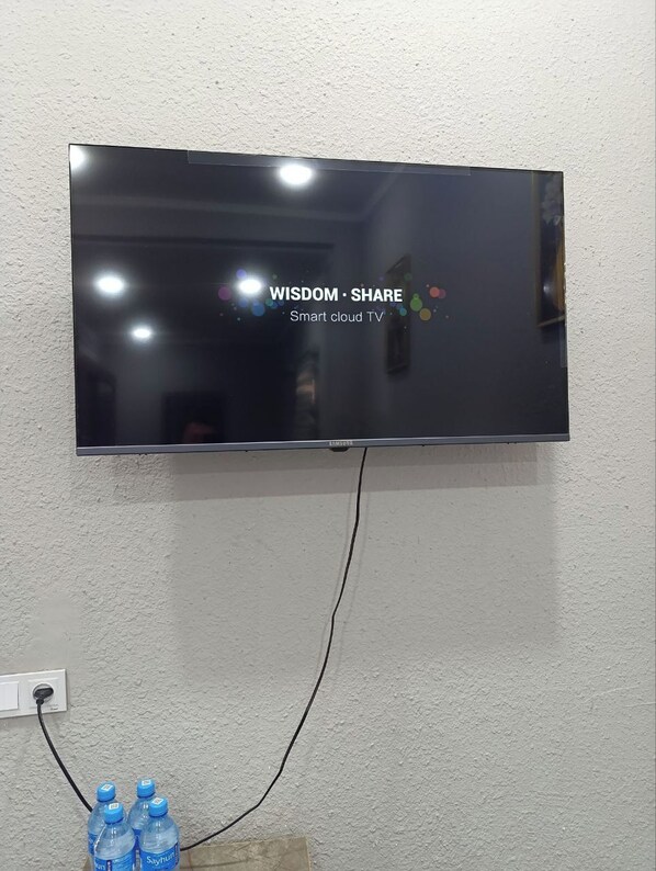 A flat-screen TV mounted on a wall with a visible power cord and a water bottle on the floor.