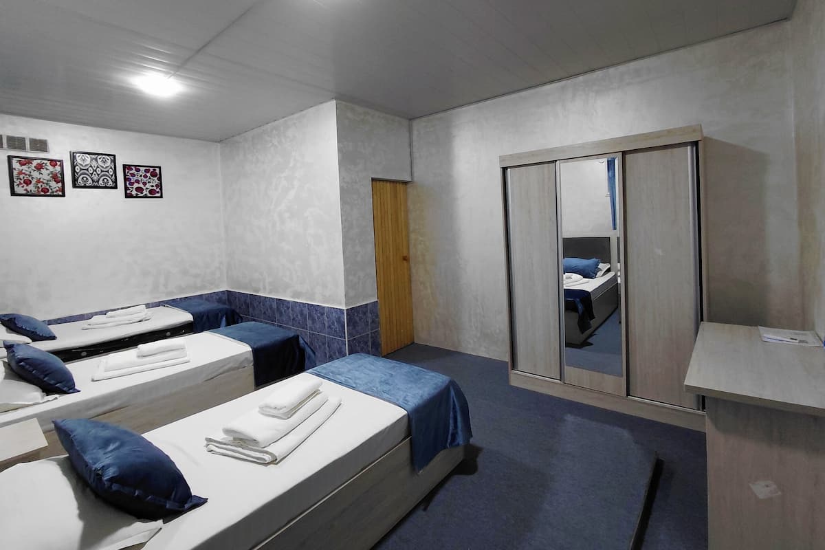 Ein Hotelzimmer mit drei Einzelbetten, einem Kleiderschrank und einem kleinen Schreibtisch.