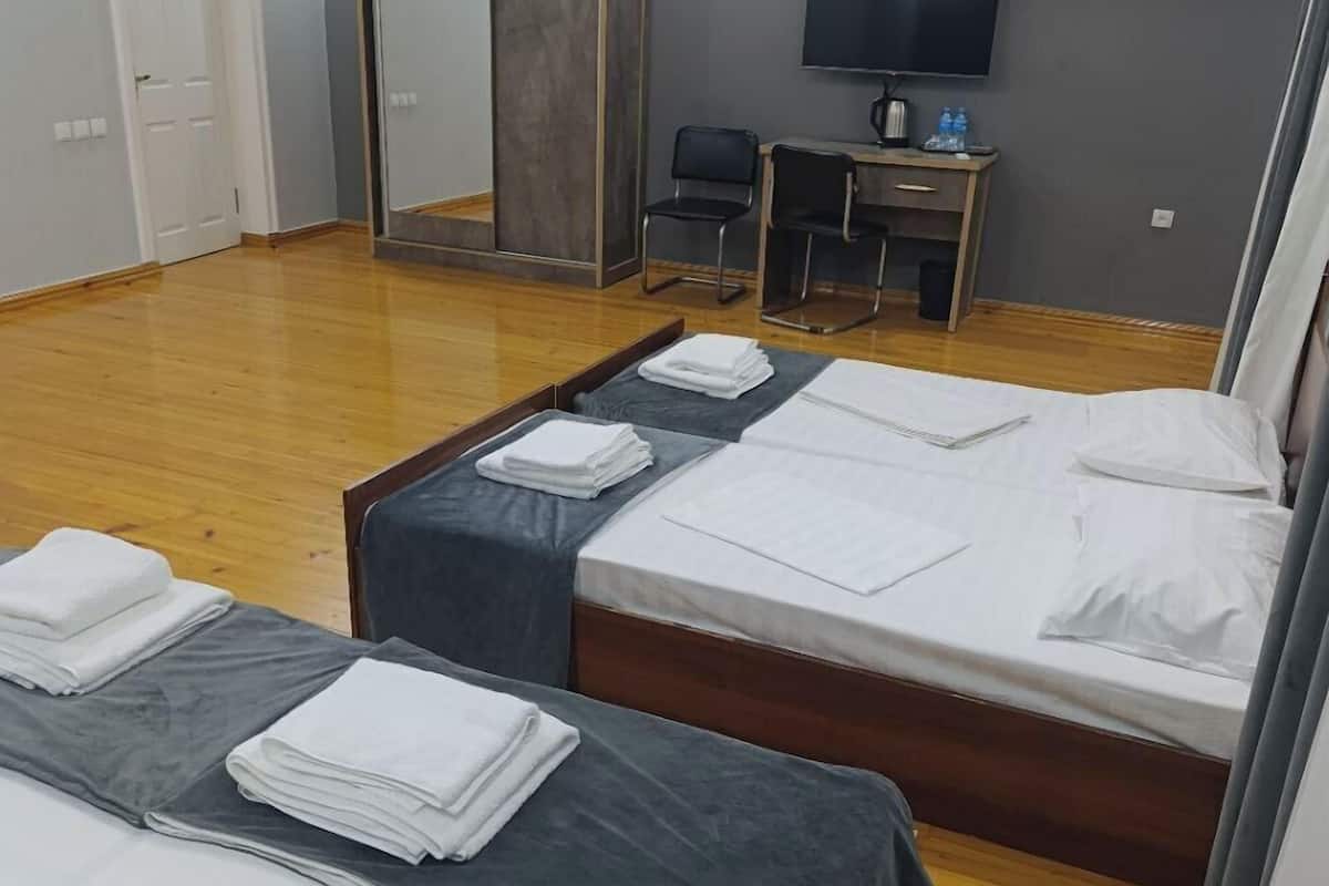 Ein Hotelzimmer mit drei Betten, einem Schreibtisch, einem Stuhl und einem Fernseher.