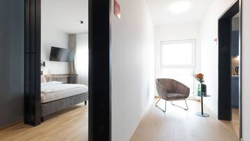 Ein modernes Hotelzimmer mit Bett, Flachbildfernseher, Sessel und einem kleinen Tisch mit Blumenvase.