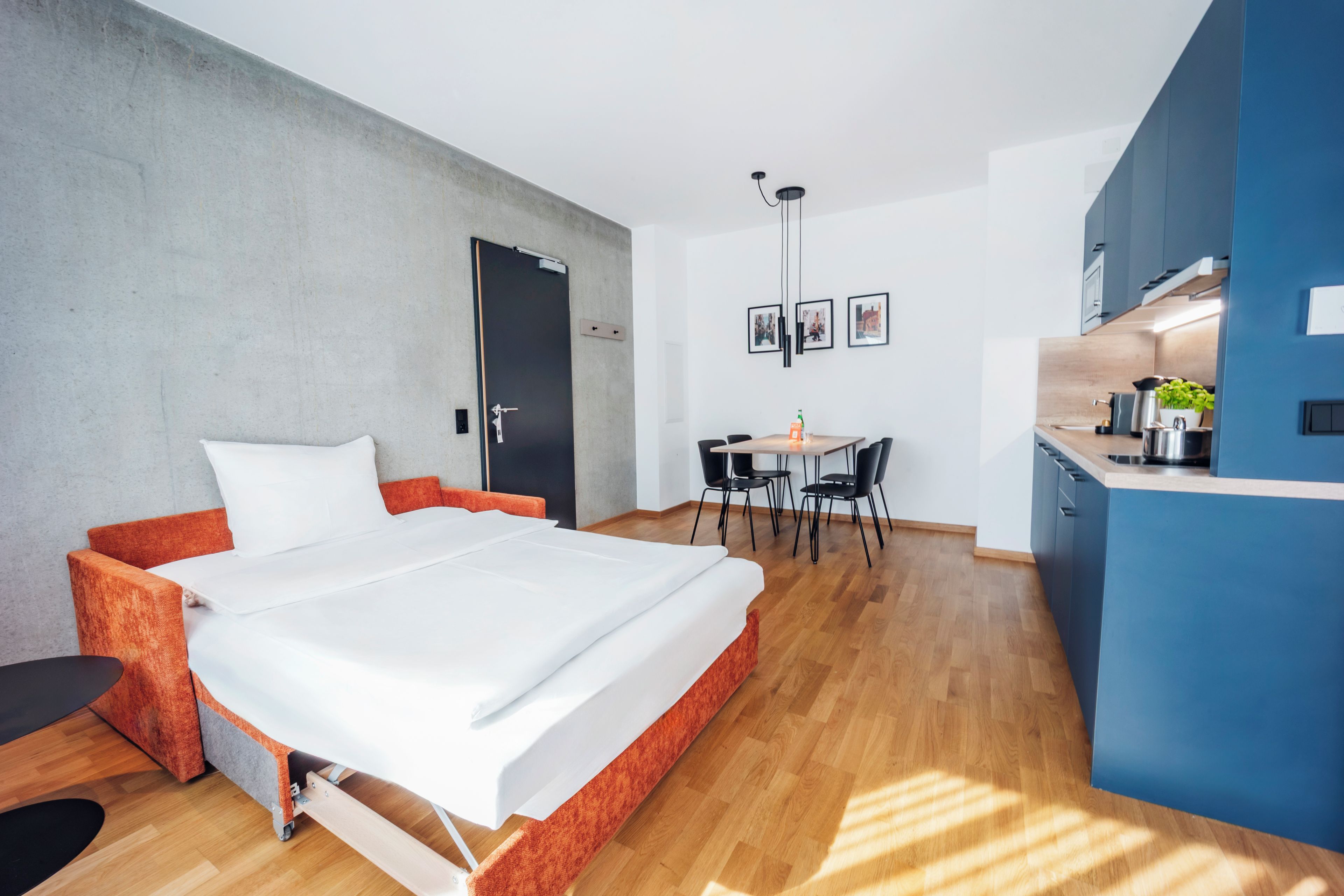 A modern bedroom with a bed, a desk, and a kitchenette.