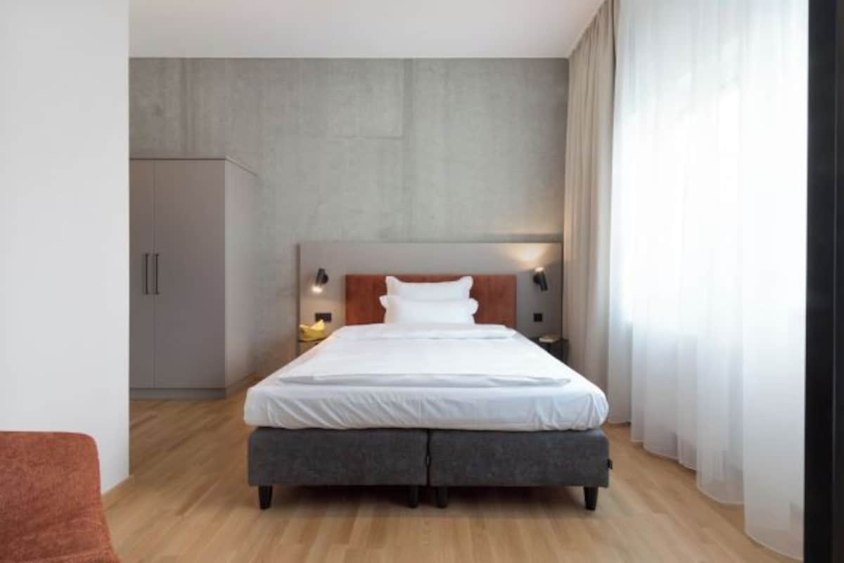 Un dormitorio moderno con una cama grande, lámparas de noche, un armario y vistas al exterior.