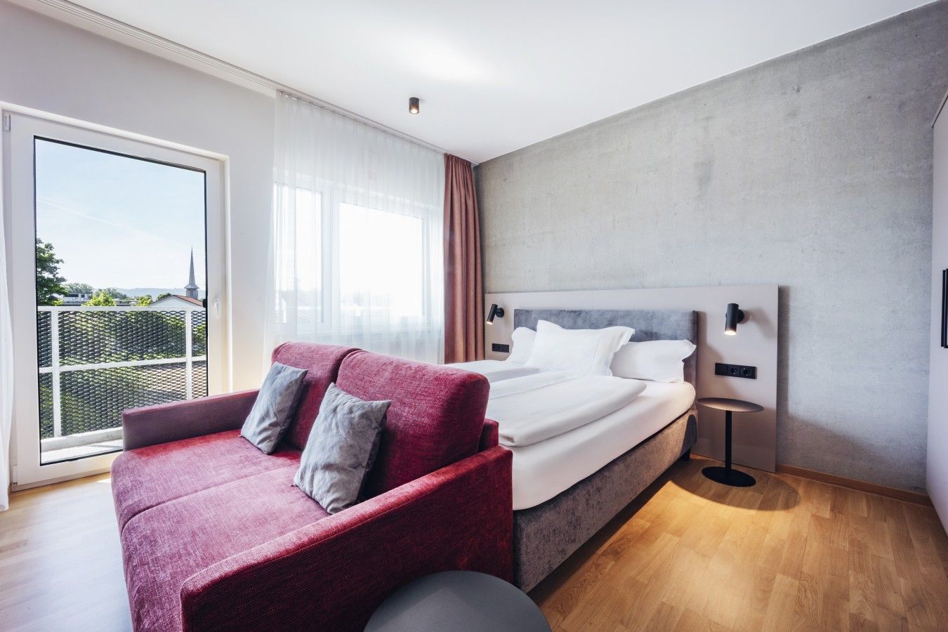 A modern bedroom with a large bed, a red sofa, and a view of the outdoors.