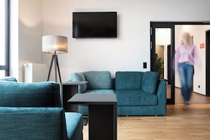 Uma sala de estar moderna com sofás verde-água, uma luminária de chão e uma televisão de tela plana na parede.
