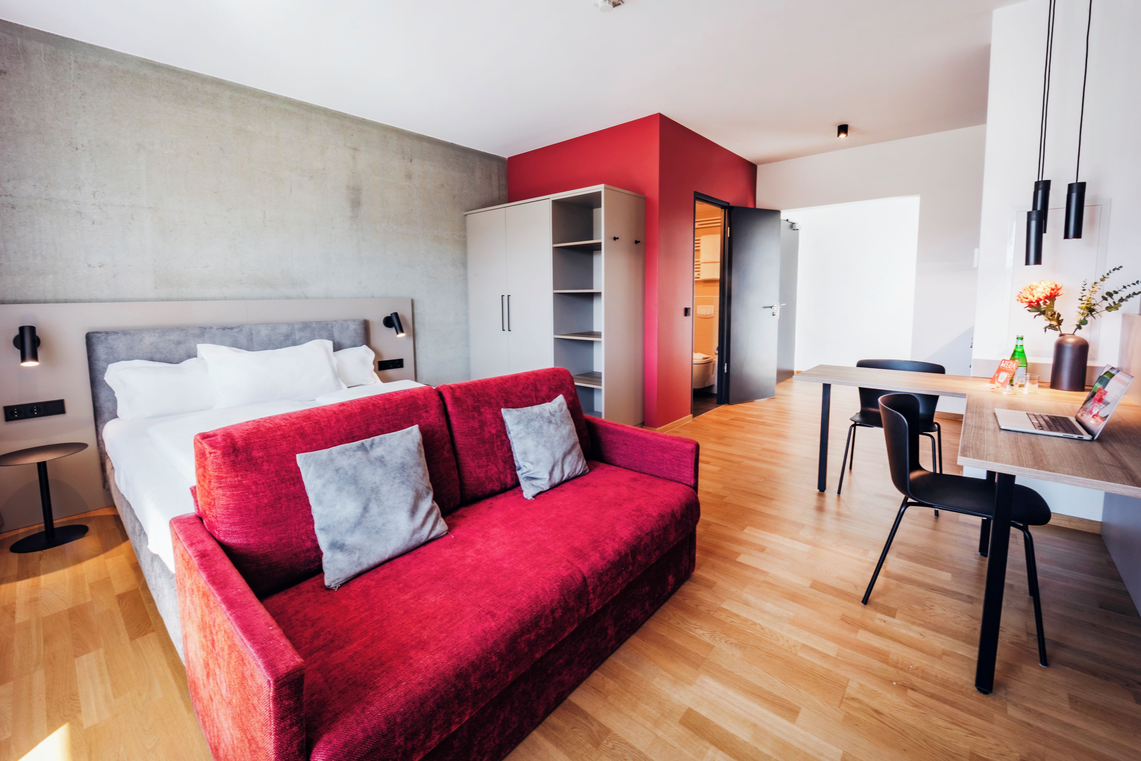 A modern living room with a red sofa, a wooden dining table, and a kitchen area.