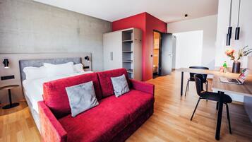 A modern living room with a red sofa, a wooden dining table, and a kitchen area.
