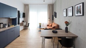 A modern kitchen with dark cabinets, a dining area with a wooden table and chairs, and a living space with a sofa and a coffee table.