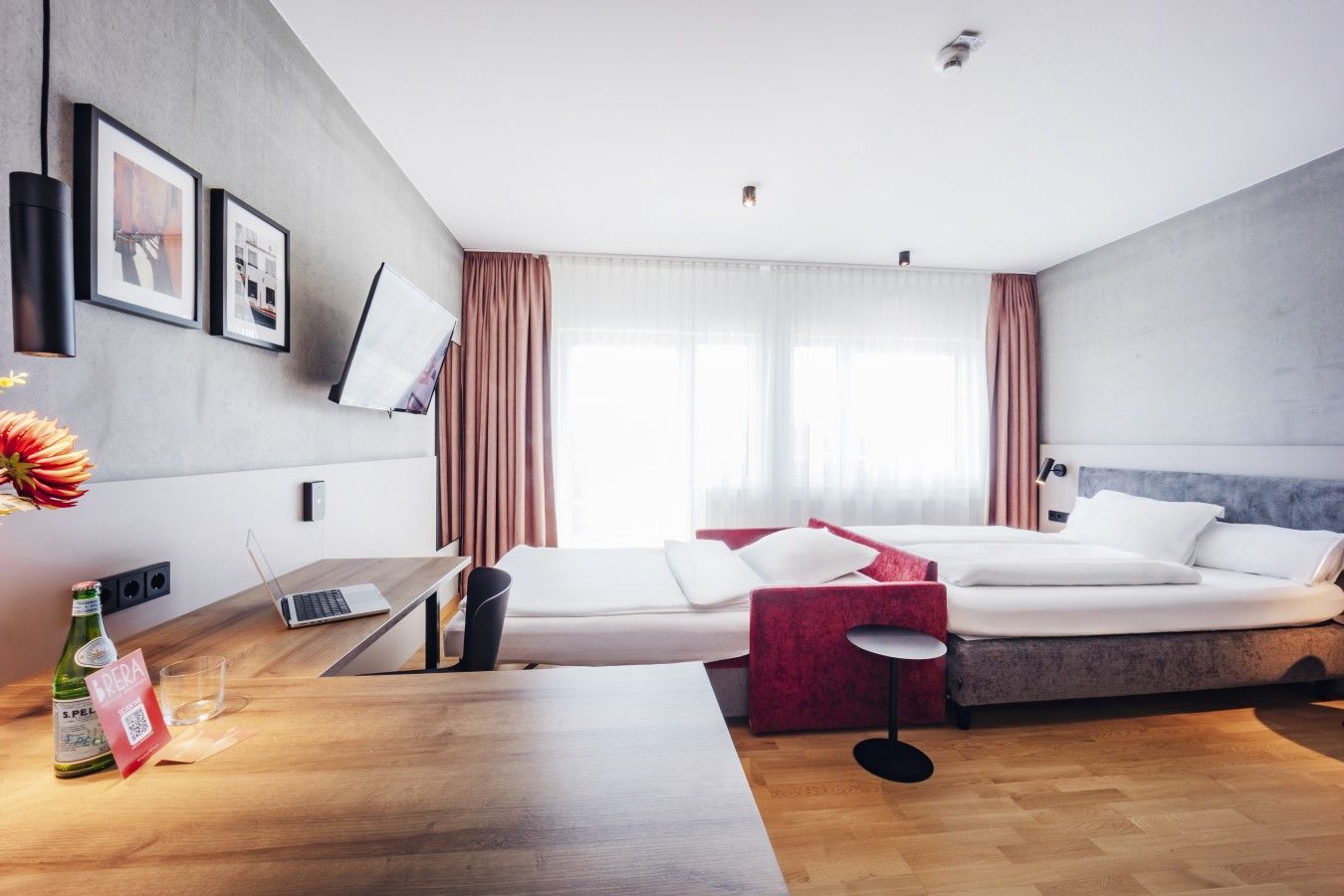 Ein modernes Hotelzimmer mit Bett, Schreibtisch, Laptop, kleinem Tisch und einer Wasserflasche.