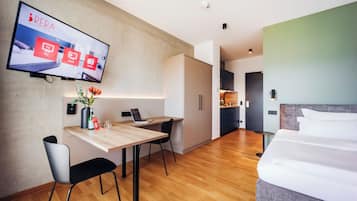 A modern hotel room with a wooden desk, a bed, and a TV mounted on the wall displaying a service interface.