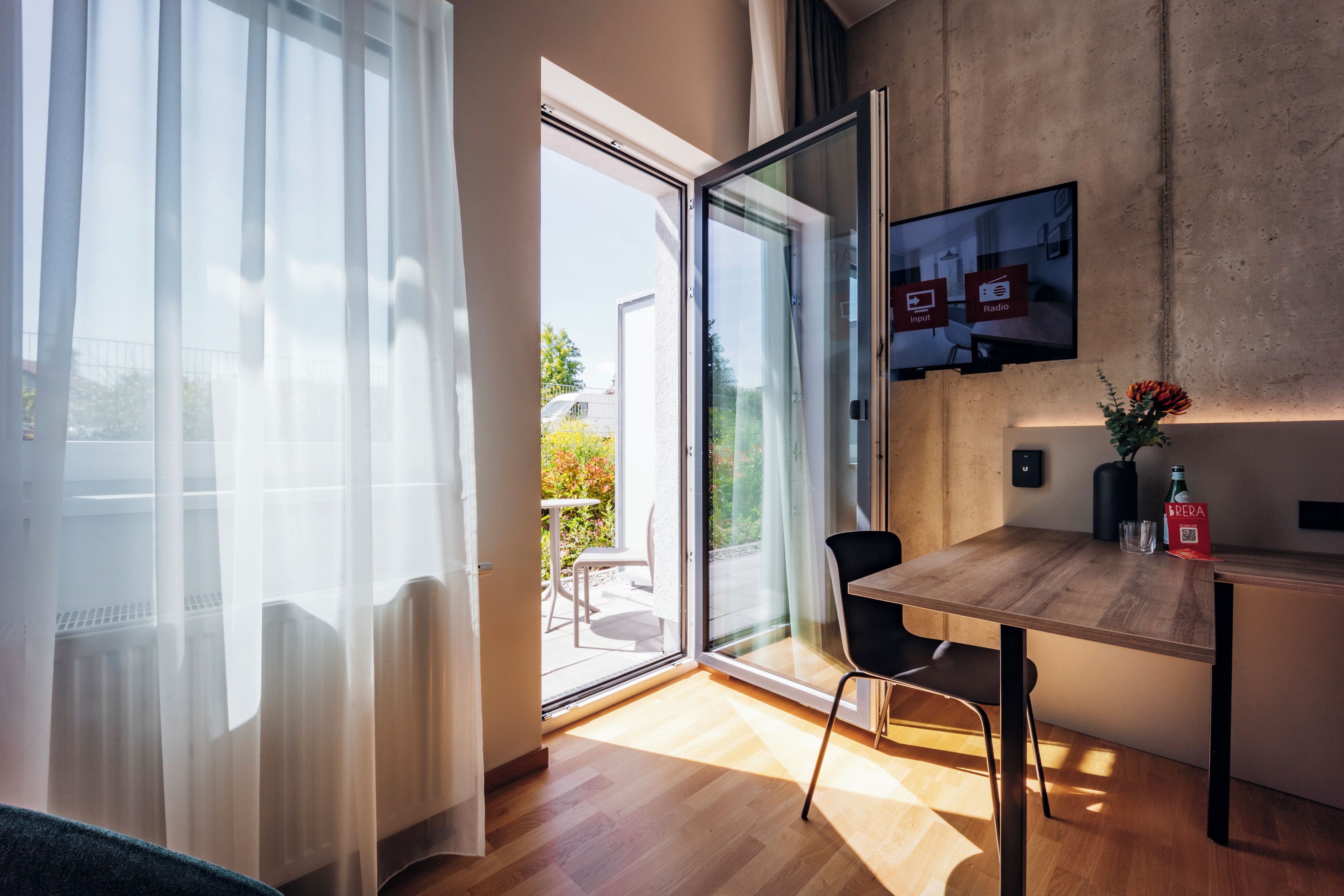 Een moderne kamer met een houten eettafel, een aan de muur bevestigde televisie en een glazen schuifdeur naar een buitenruimte.