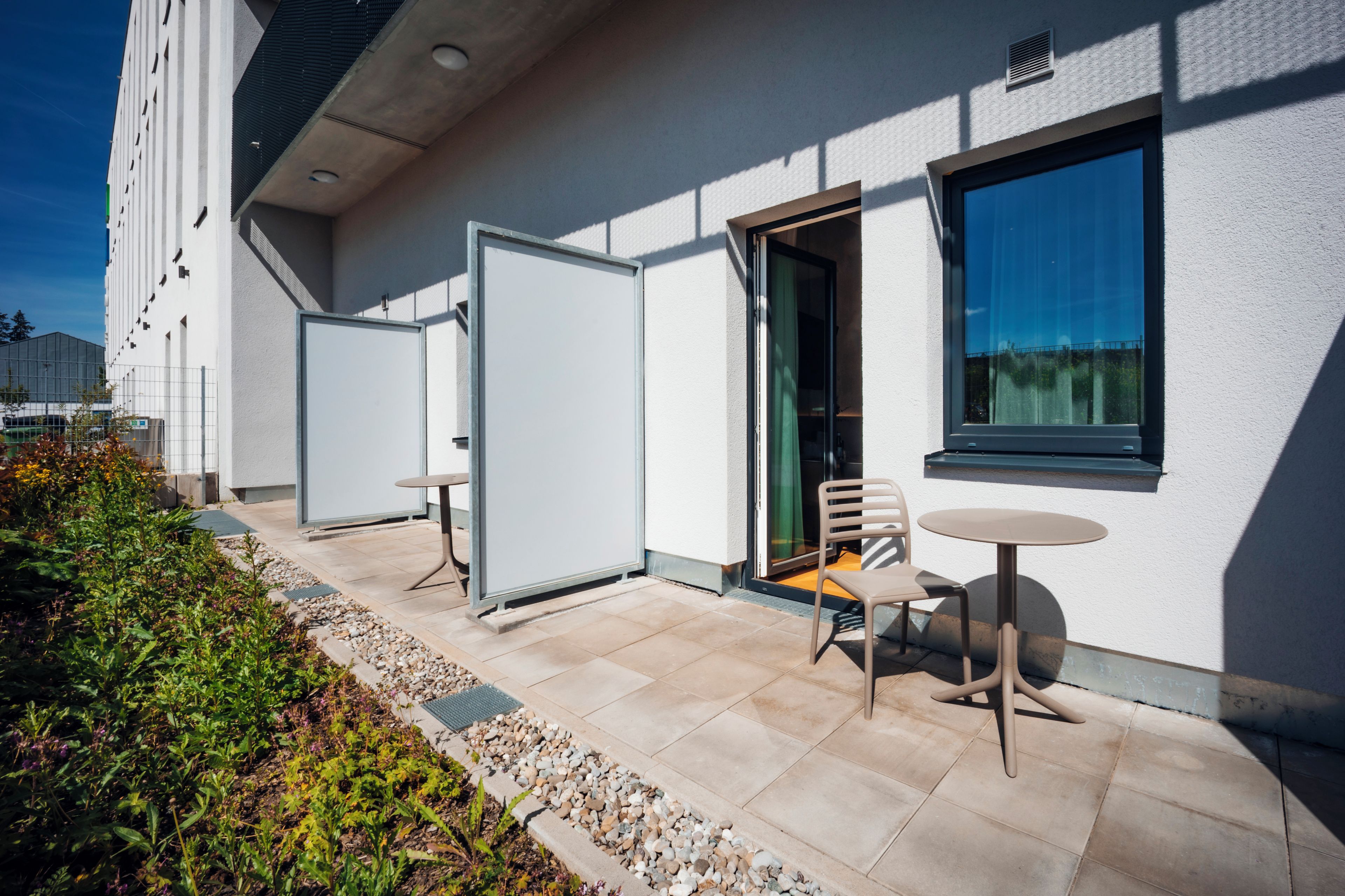Un área de estar exterior moderna con una mesa, sillas, una puerta y una ventana.