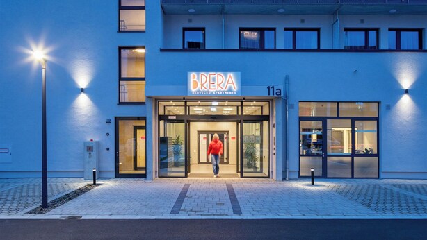 A serviced apartment building named 'BRERA' with a modern design, large glass windows, and a well-lit entrance.