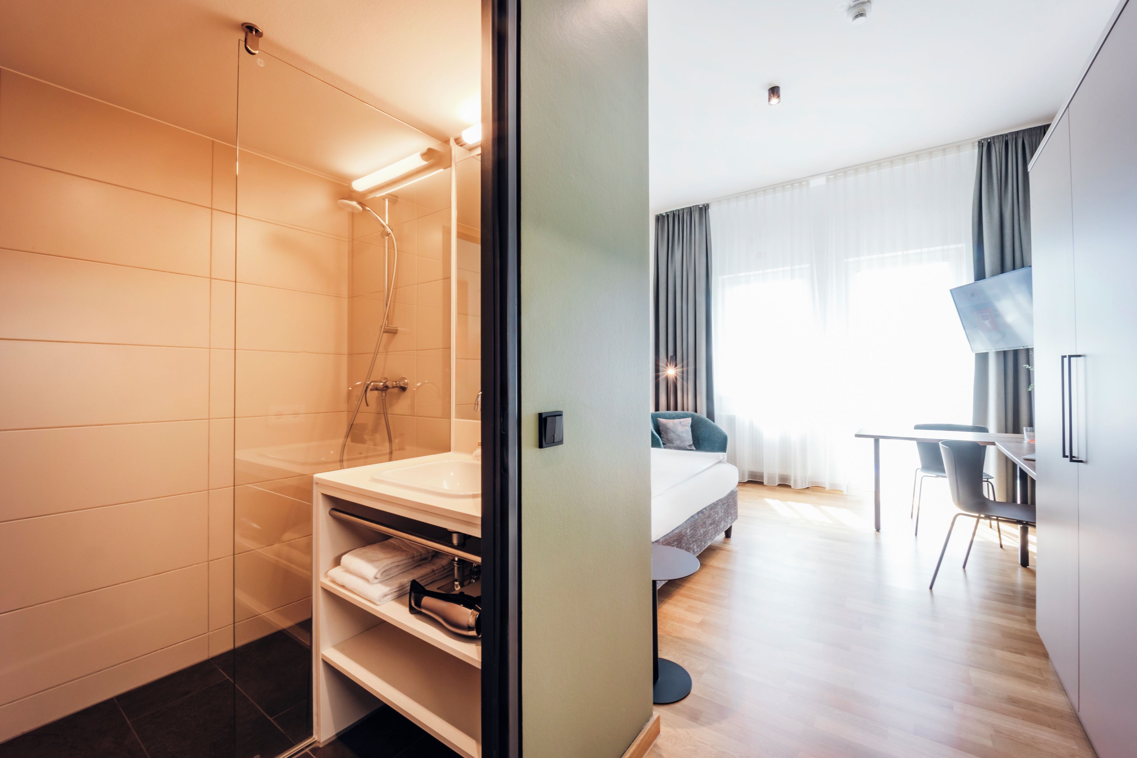 A modern hotel room with a shower, a bed, a desk, and a TV.