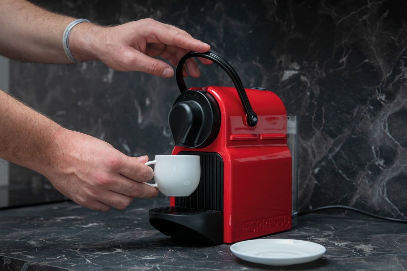 Una persona usando una máquina de café espresso roja y negra sobre una encimera de mármol.