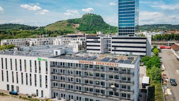 Un immeuble à plusieurs étages, doté d’un toit plat, portant l’inscription « APPARTEMENTS AVEC SERVICES », et comprenant une rangée de balcons ainsi qu’un espace de stationnement.