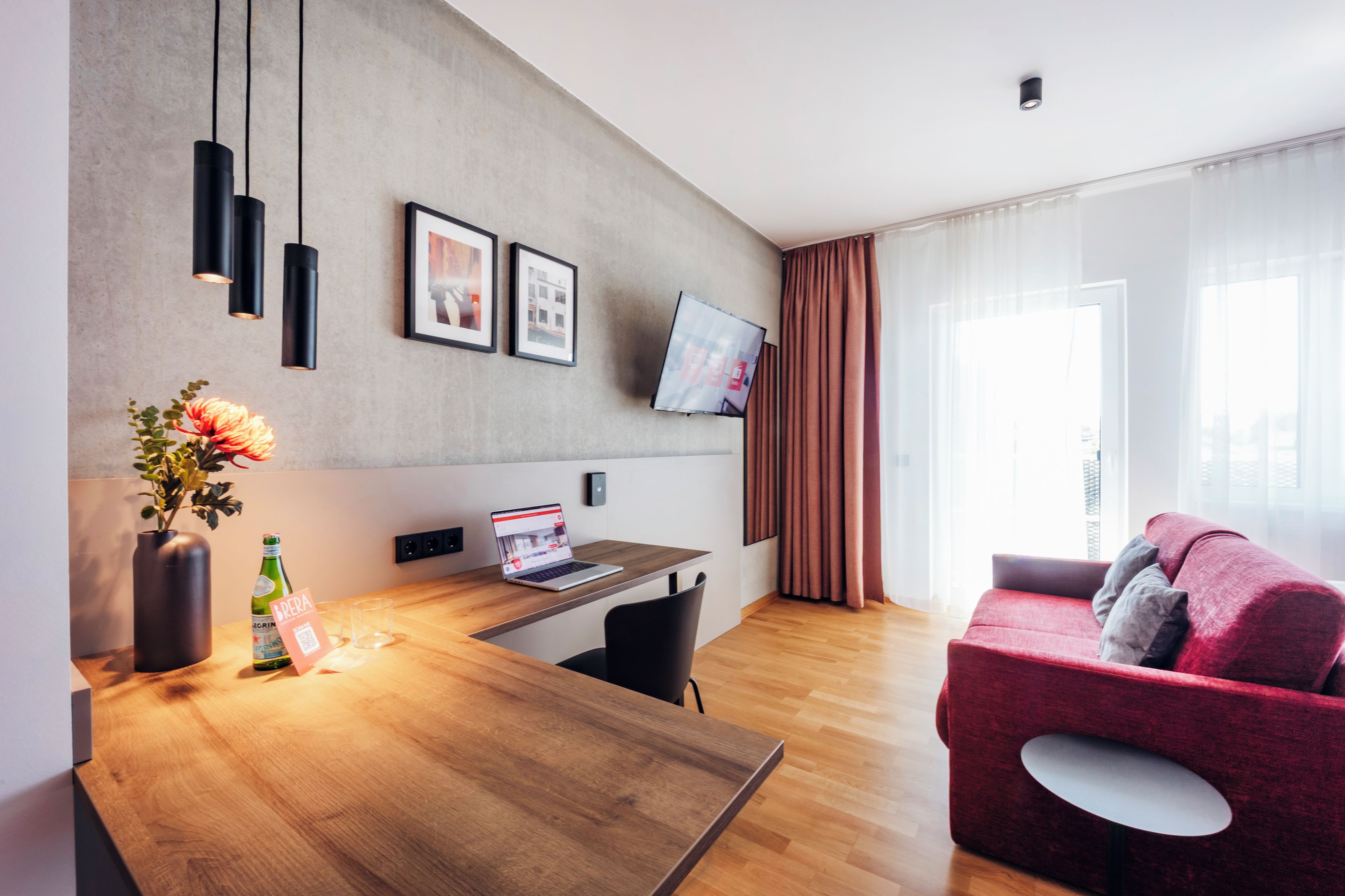 A modern living space with a wooden dining table, a red sofa, and a flat-screen TV mounted on the wall.