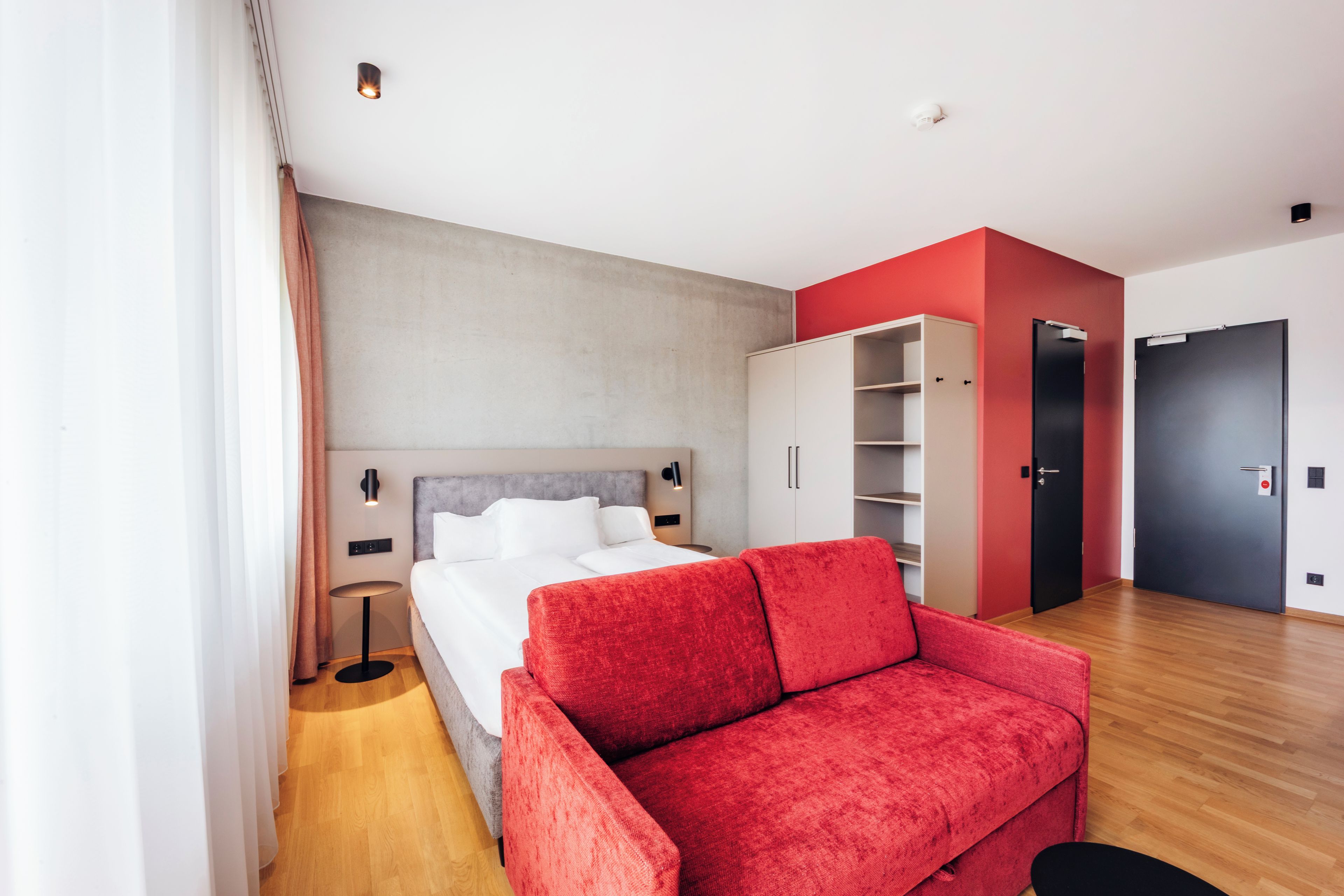 Una habitación de hotel moderna con cama, sofá rojo, armario y puerta.