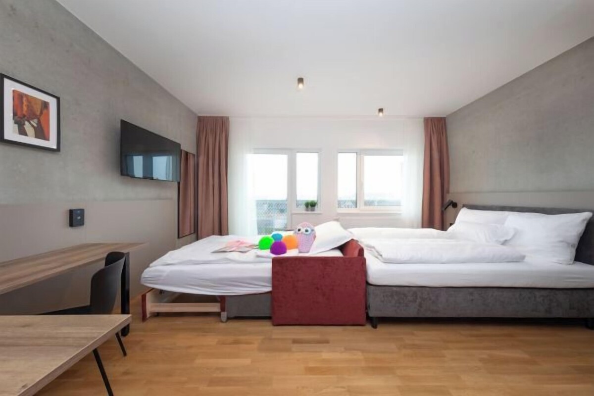 Una habitación de hotel moderna con cama, escritorio, televisión y ventana con cortinas.