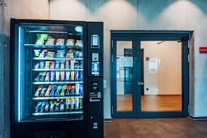 Máquina expendedora llena de bocadillos y bebidas, una puerta con panel de vidrio y un cartel que indica 'Apartments 001-004'.