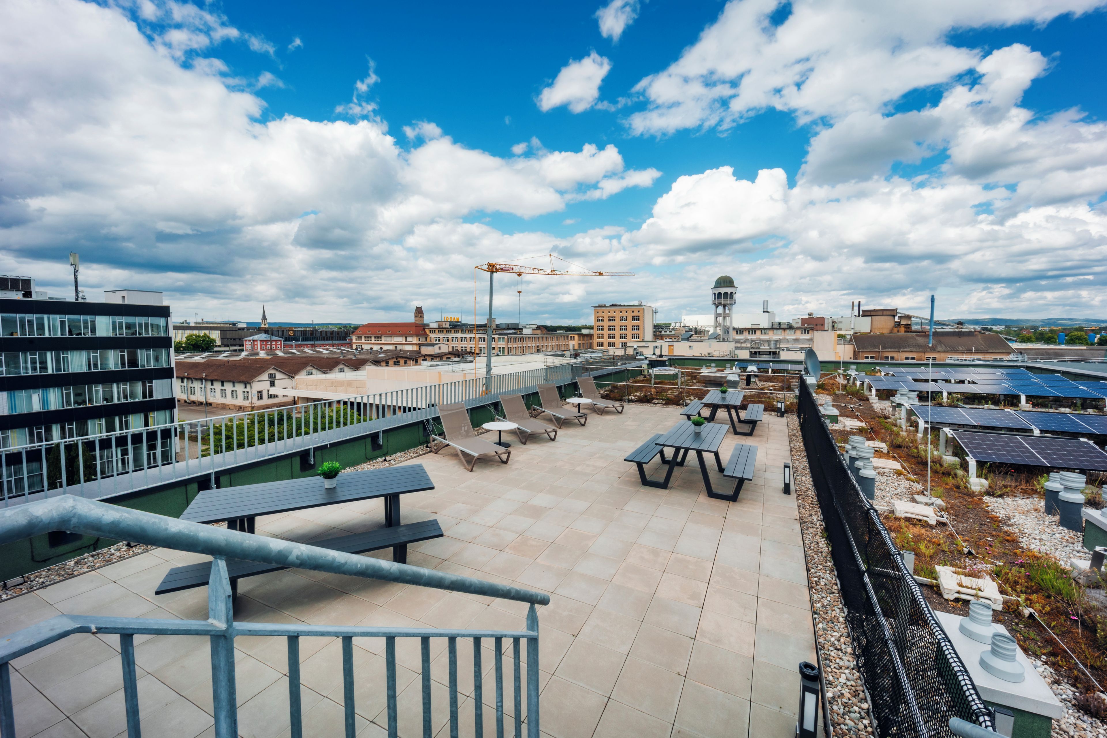 Eine Dachterrasse mit Sitzgelegenheiten im Freien, Solaranlagen und Blick auf die Stadtlandschaft.