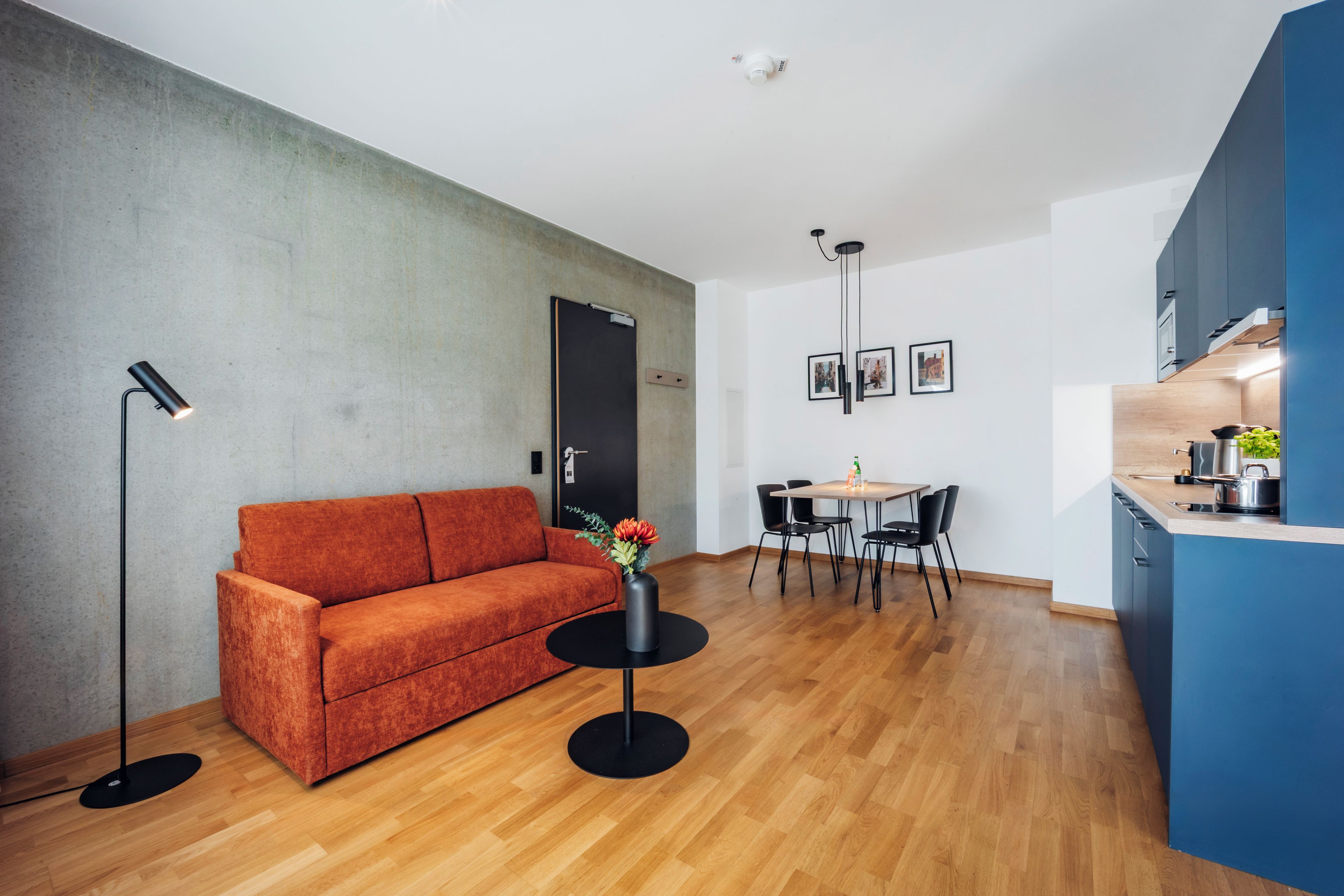 Een moderne woonruimte met een bank, een eettafel met stoelen, een klein rond tafeltje met een vaas en een kitchenette.