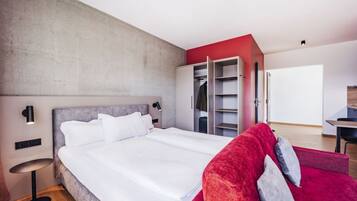 A modern bedroom with a large bed, a wardrobe, a desk, and a red sofa.