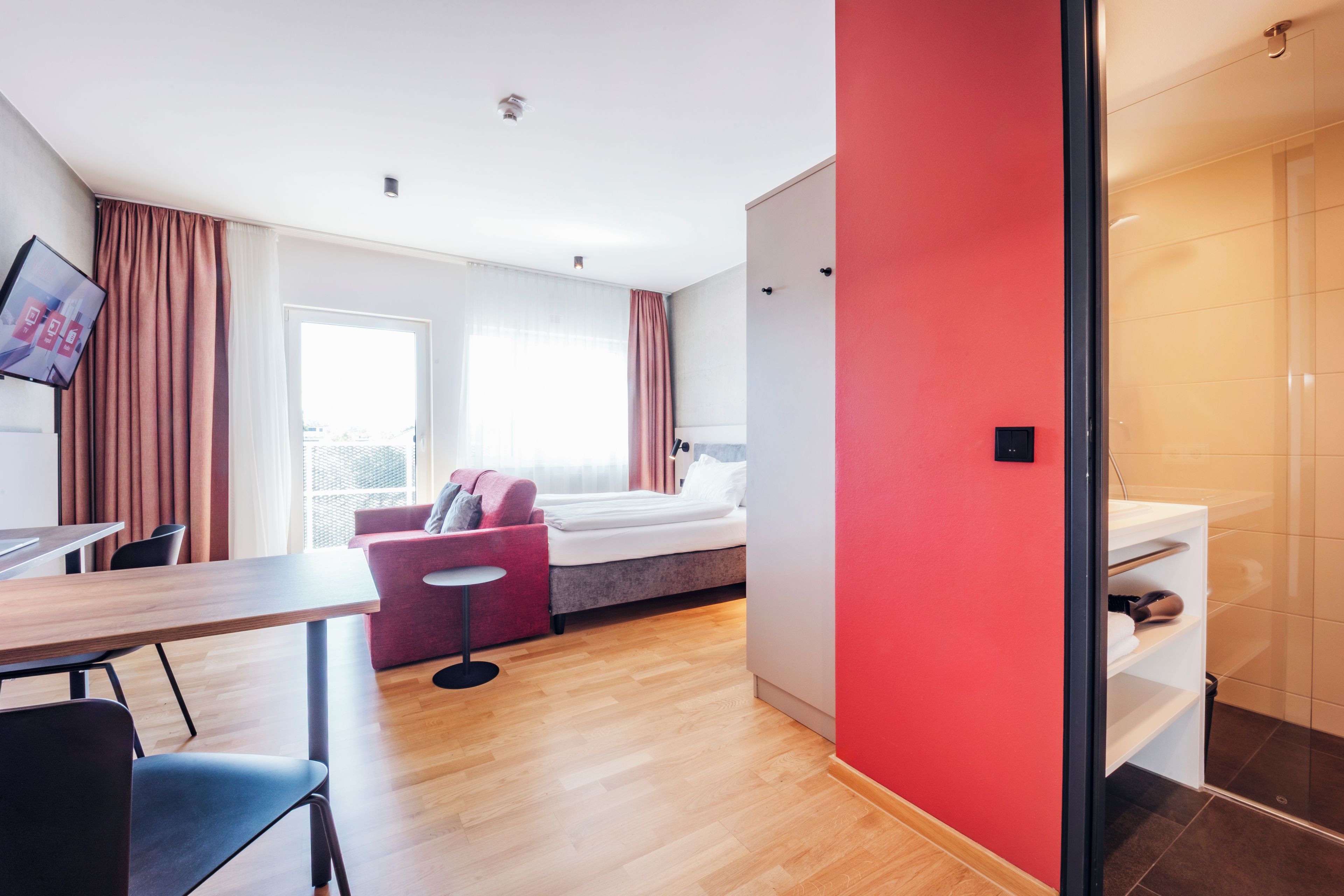 Una habitación de hotel moderna con una cama, un pequeño rincón de descanso, un escritorio y vistas al exterior.