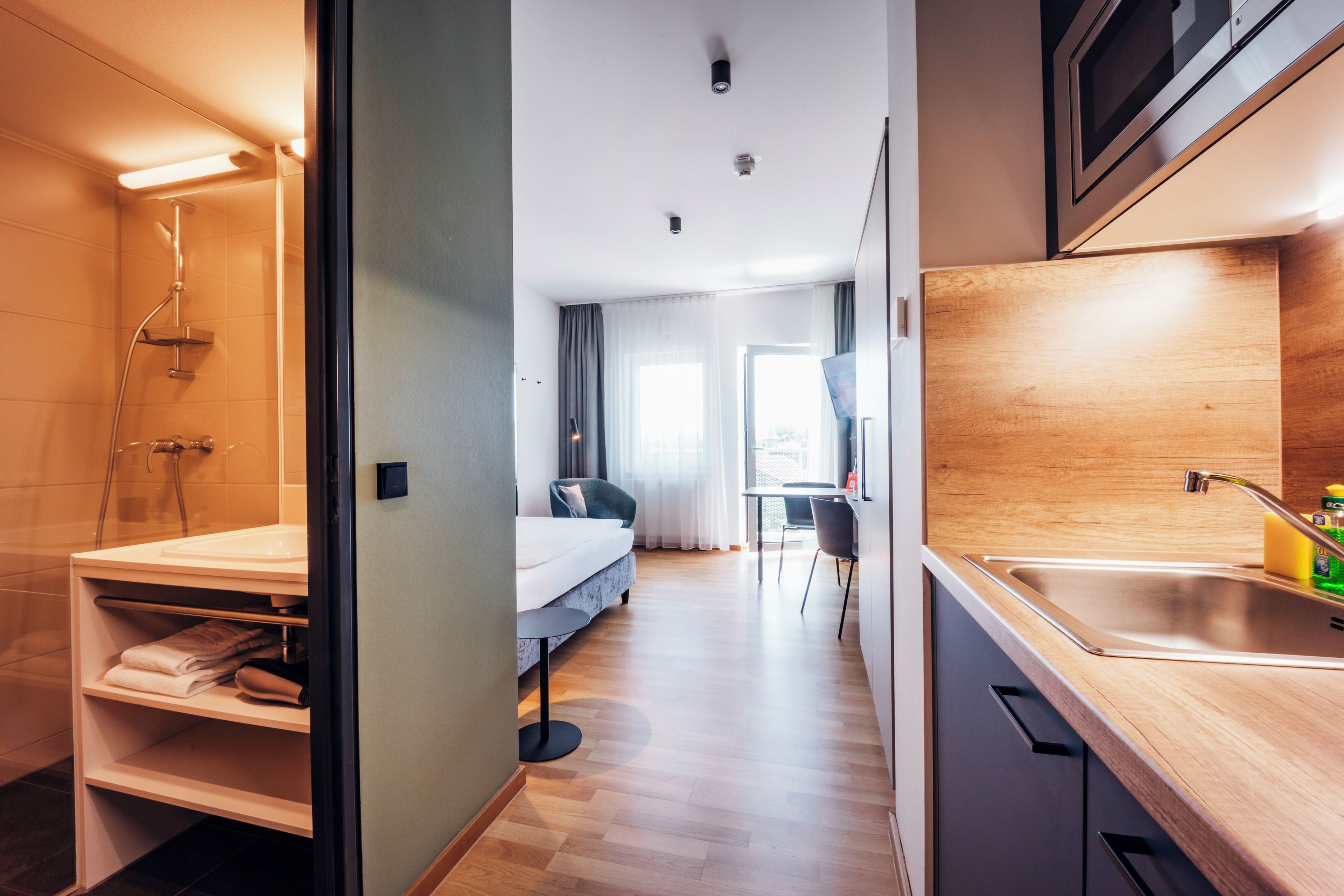 Een kleine hotelkamer met een douche, een bed, een tafeltje en een kitchenette.