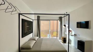 Ein modernes Hotelzimmer mit Bett, Fernseher, Balkon und Blick ins Freie.