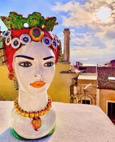 A bust with a decorative headpiece and jewelry, set against a cityscape with buildings and a clear sky.