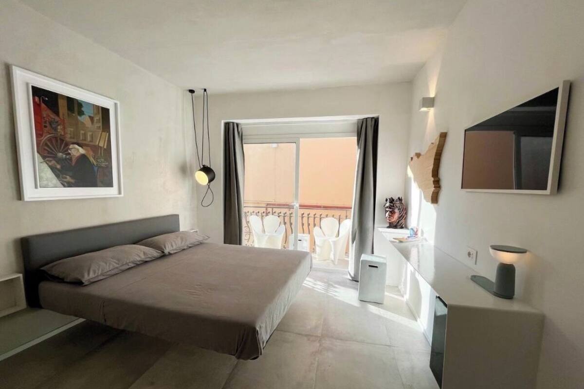 Een moderne hotelkamer met een groot bed, een balkon met witte stoelen, een klein bureau en een wandgemonteerde televisie.