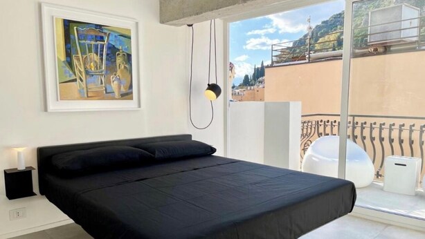 Een moderne slaapkamer met een groot bed, een nachtkastje, een lamp en een schilderij aan de muur.