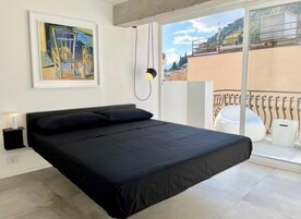 A modern bedroom with a large bed, a bedside table, a lamp, and a painting on the wall.