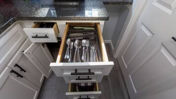 A kitchen with white cabinets, a granite countertop, and a drawer organizer containing silverware.