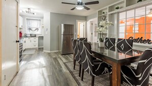 Una cocina moderna con armarios blancos, un refrigerador de acero inoxidable y un comedor con mesa de vidrio y sillas blancas y negras.