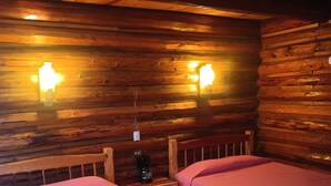 Une chambre de style cabane avec deux lits, des murs en bois et des lampes fixées au mur.