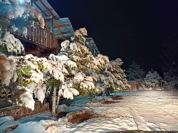 A snow-covered outdoor area with a wooden deck and a building with a metal roof. - Room-parador Arewá 1 La Energía Que Impu (Bocoyna)