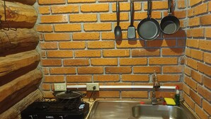 Une cuisine de taille réduite avec un mur en briques, une cuisinière à gaz, un évier et des ustensiles de cuisine suspendus.