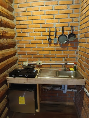 A compact kitchen with a brick wall, a gas stove, a sink, and hanging cookware. - Room-parador Arewá 1 La Energía Que Impu (Bocoyna)
