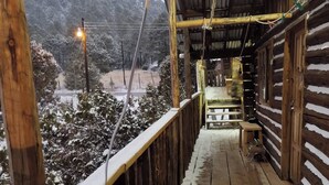 Une cabane en bois dotée d’un porche abrité, d’un banc et offrant une vue sur un paysage enneigé.