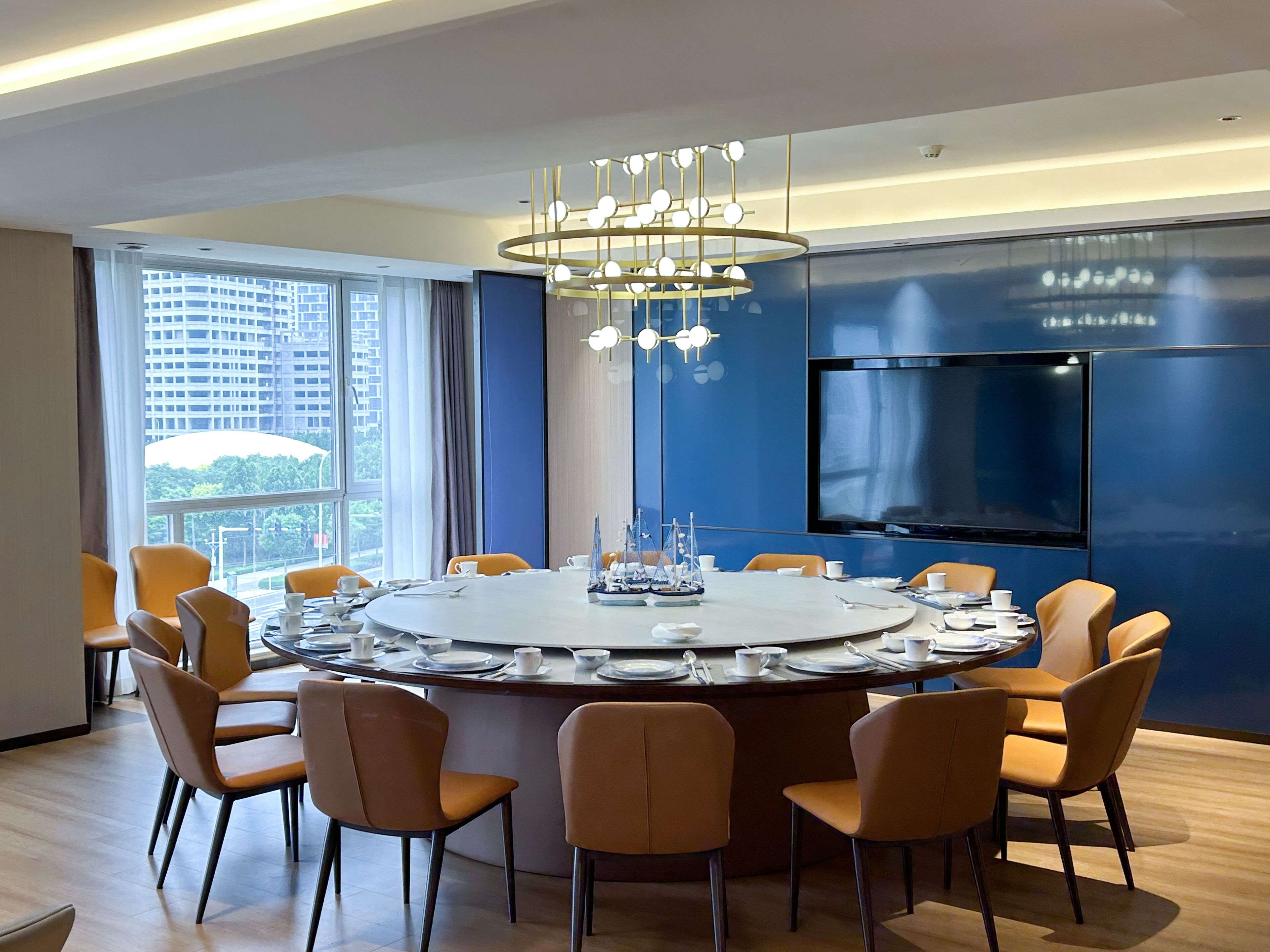 A modern conference room with a round table, chairs, a chandelier, and a large TV screen.