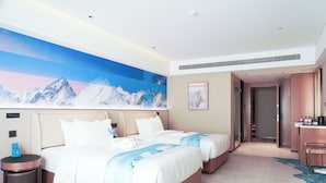 Quarto de hotel com duas camas, uma grande pintura de uma paisagem montanhosa, uma mesa com uma cadeira e uma lixeira.