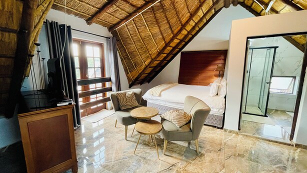 A cozy attic bedroom with a sloped ceiling, a bed, a seating area with a small table, and a wardrobe. - Pretoria Mansion Boutique Hotel (Pretoria)