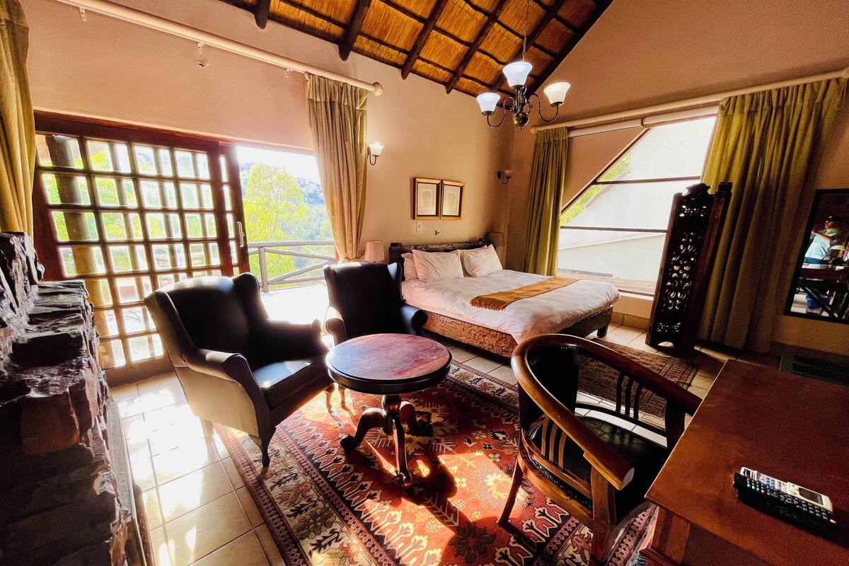 A room with a bed, two chairs, a small table, a TV, and a balcony with a view.