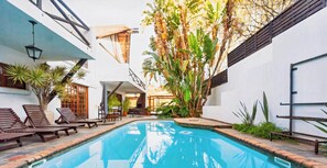 A swimming pool with lounge chairs, a covered seating area, and lush tropical plants. - Pretoria Mansion Boutique Hotel (Pretoria)