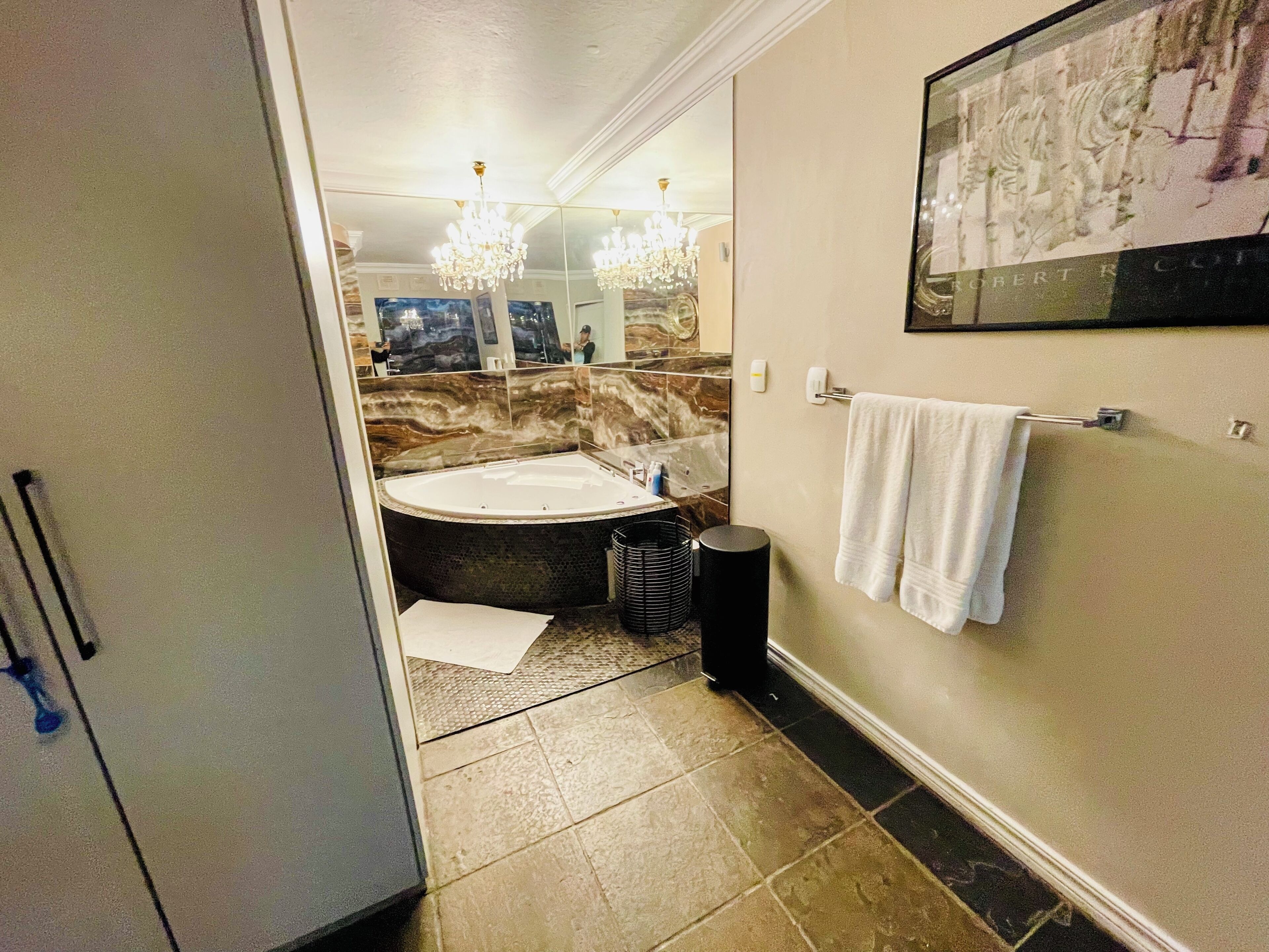 A bathroom with a large bathtub, a mirror, a chandelier, and a towel rack.