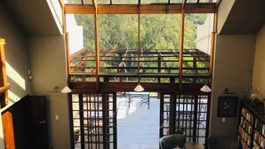 A room with a high ceiling, wooden beams, a view of greenery outside, a seating area with a table and chairs, and a bookshelf. - Pretoria Mansion Boutique Hotel (Pretoria)