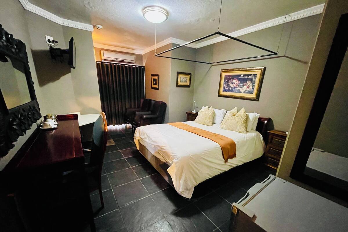 A hotel room with a bed, a desk, a chair, a TV, and a painting on the wall.